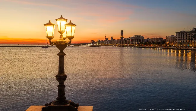 Three-lantern street lamp at dawn by the sea in Bari